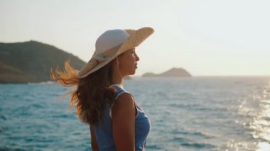 Yazlık elbiseli kadın gün batımında kıyıda duruyor, resimli deniz manzarasına hayran.