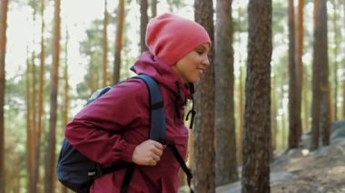 Sırt çantalı çekici genç bir kadının portresi çam ormanında yürüyor, etrafına bakıyor, gülümsüyor. Mutlu Kafkas kadın turistler doğaya hayranlıkla bakıyor Trekking yürüyüş gezisi, güneşli bir gün