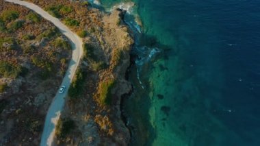 Hava manzaralı, sahil yolunda araba sürüyor, deniz dalgaları kayalık kıyıları yıkıyor.