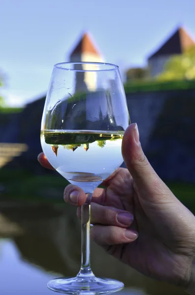 Een glas witte wijn in een hand met een kasteel weerspiegelen in. — Stockfoto