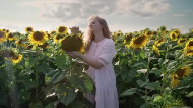 Ayçiçeği tarlasında oturan sarışın beyaz kız telefonda poz veriyor.