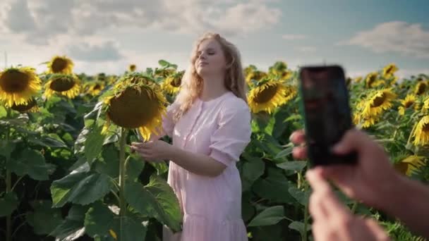 Menina loira em um campo de girassol lê livro, posando no telefone para cara bonito — Vídeo de Stock