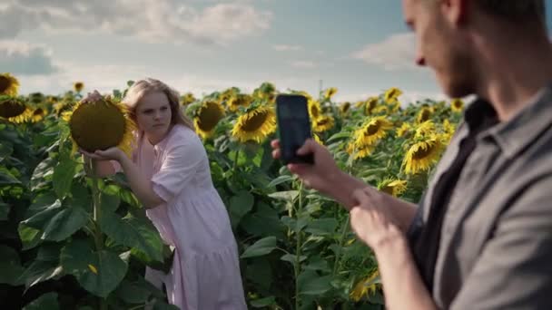 Blonde fille dans un champ de tournesol lit livre, posant au téléphone pour mignon gars — Video