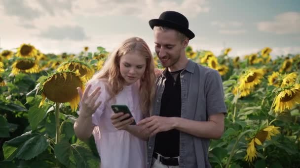 Пара девушка с парнем на подсолнечном поле на фотосессии выбирают фотографии на телефон — стоковое видео