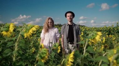 Ayçiçeği tarlasında beyaz bir kız telefon kamerasında şapkalı bir adamla poz veriyor.