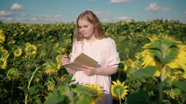Young blonde female in sunflower field reads book, guy in hat closes girls eyes — Stock Video