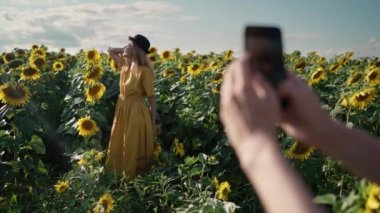 Ayçiçeği tarlasında fotoğraf çekiminde telefonla fotoğraf çeken kızıl saçlı bir kadın.