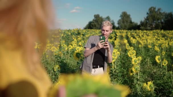 Wanita berambut merah di bidang bunga matahari difoto pada pria telepon di topi — Stok Video
