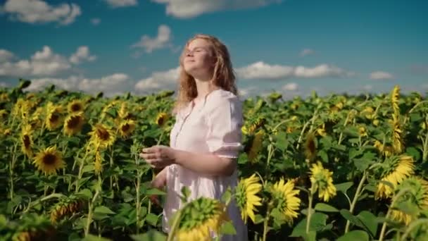 해바라기 밭에서 미소를 짓고 곱슬곱슬 한 머리를 하고 있는 금발의 백인 여성 — 비디오