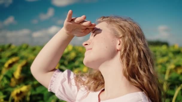 Jong blond Kaukasisch meisje in zonnebloem veld glimlacht, rechte krullend haar — Stockvideo