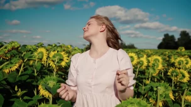 Young blonde caucasian girl with curly hair walks in sunflower field smiles — Stock Video