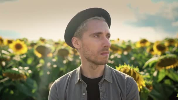 Młody biały facet w czarny kapelusz w słonecznik pole w słoneczny dzień — Wideo stockowe