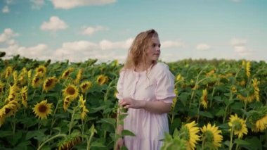 Ayçiçeği tarlasında genç sarışın beyaz kız gülümsüyor, kıvırcık saçları düzleştiriyor.