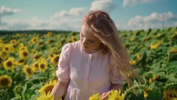 Junge blonde kaukasische Mädchen in Sonnenblumenfeld lächelt, glätten lockiges Haar — Stockvideo