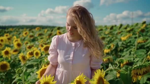 Молодая блондинка-кавказка с вьющимися волосами на подсолнечном поле улыбается — стоковое видео