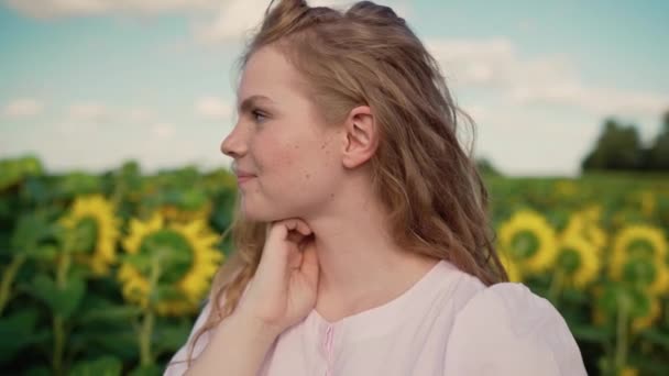 Young blonde caucasian girl in sunflower field smiles, straighten curly hair — Stock Video