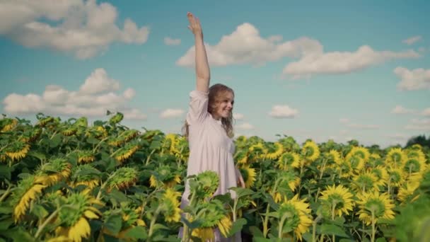 Молодая блондинка-кавказка на подсолнечном поле улыбается, выпрямляет вьющиеся волосы — стоковое видео