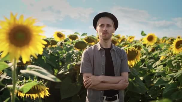 Junger kaukasischer Typ mit schwarzem Hut in einem Sonnenblumenfeld an einem sonnigen Tag — Stockvideo