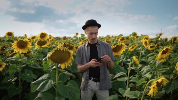 Jong guy met, doorboord in een zonnebloem veld neemt een selfie op de telefoon camera — Stockvideo