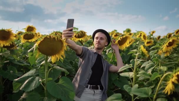 Mladý chlap s, propíchnutý na slunečnicovém poli vezme selfie na fotoaparátu — Stock video