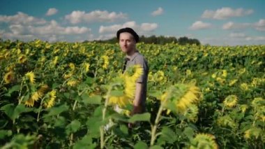 Ayçiçeği tarlasında güneşli bir günde siyah şapkalı genç beyaz adam.