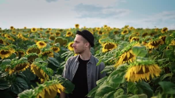 Mladý kavkazský chlap v černém klobouku na slunečnicovém poli v slunečný den — Stock video