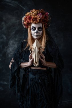 Ağzı dikilmiş cadılar bayramı cadısı, boynuzları, karanlık bir odada kafatası,