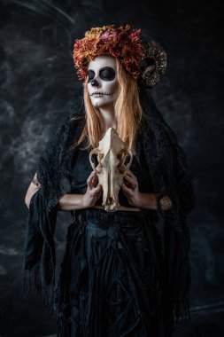 Ağzı dikilmiş cadılar bayramı cadısı, boynuzları, karanlık bir odada kafatası,