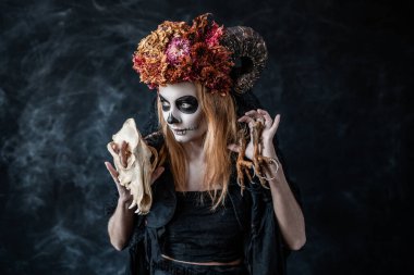 Kafatası olan cadılar bayramı cadısı, karanlık odada boynuzlar beliriyor, kötü niyetle gülümsüyor.