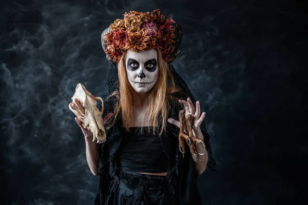 Halloween witch with skull, horns conjures in a dark smoky room, looks at camera — Stock Photo, Image