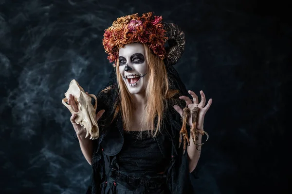 Απόκριες μάγισσα με κρανίο, κέρατα πλέκει στο σκοτεινό δωμάτιο, γελάει κακόβουλα — Φωτογραφία Αρχείου
