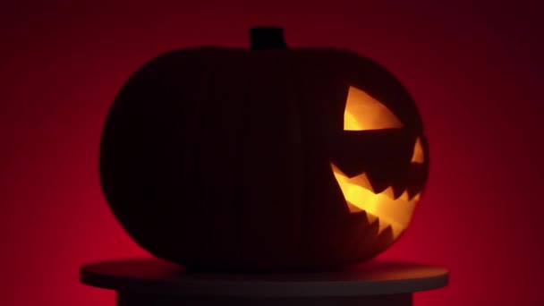 Halloween pompoen met dinamik licht op draaiend platform, rode achtergrond — Stockvideo