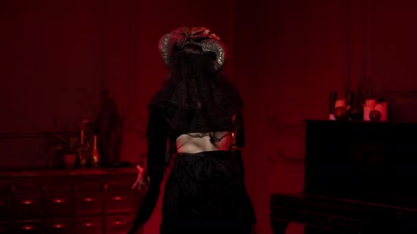 Mujer bruja para halloween con calavera cráneo maquillaje, cuernos en una habitación de color rojo oscuro — Vídeo de stock