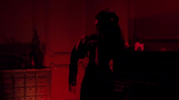 Bruxa com chifres, flores secas danças em um quarto vermelho escuro para flashes de luz — Vídeo de Stock