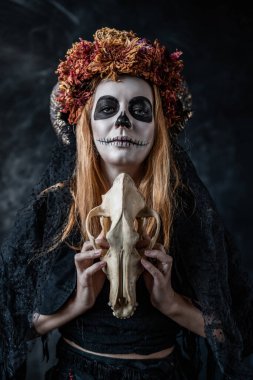 Ağzı dikilmiş cadılar bayramı cadısı, boynuzları, karanlık bir odada kafatası,