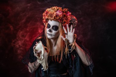 Cadılar Bayramı 'nda boynuzları, kafatası ve kırmızı odada kuş pençeleri olan cadı imajı olan bir kadın.