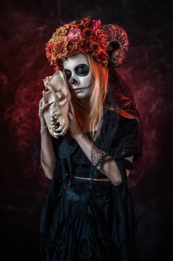 Cadılar bayramında boynuzlu bir kadın, kırmızı odada canavar kafatası.