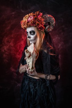 Cadılar bayramında boynuzlu bir kadın, kırmızı odada canavar kafatası.