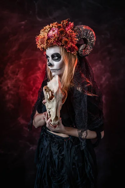 Cadılar bayramında boynuzlu bir kadın, kırmızı odada canavar kafatası.