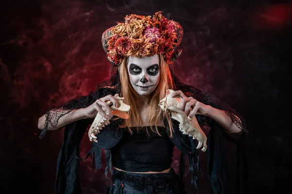 Halloween monster in skull make-up with horns tears apart the skull of a beast — Stock Photo, Image