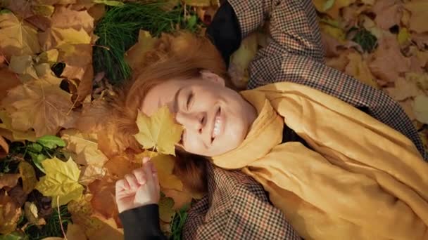 Rudowłosa kobieta w średnim wieku cieszy się jesiennym parkiem leżącym na trawie — Wideo stockowe