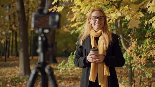 Κοκκινομάλλα γυναίκα 30-35 με φλιτζάνι τσάι καταγράφει βίντεο έκθεση σε ηλιόλουστο πάρκο φθινόπωρο — Αρχείο Βίντεο