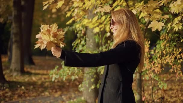 Kobieta spaceruje po jesiennym lesie, robi zdjęcia bukietem liści, uśmiecha się — Wideo stockowe