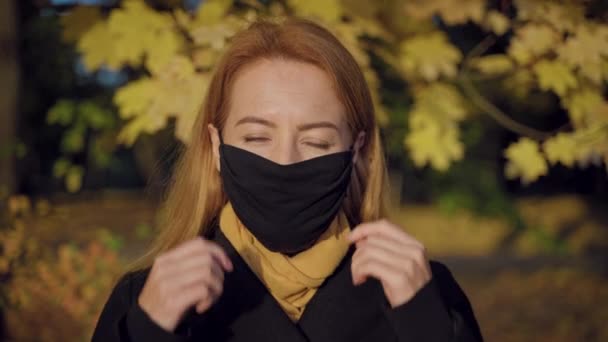 Vrouw verwijdert een beschermend masker, sluit haar ogen, geniet van frisse lucht van de herfst — Stockvideo
