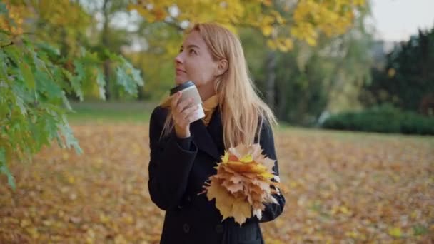 女性は紅葉の花束やコーヒーを片手に秋の広場を歩き — ストック動画