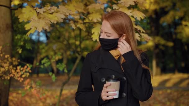 女人们摘下防护面具，在秋天的公园里喝茶，微笑 — 图库视频影像