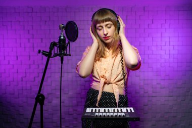 Stüdyo kulaklıklı kız gözlerini kapattı, mikrofonlu müzik dinliyor, anahtarları var.