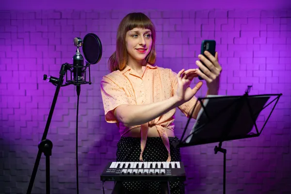 musician looks at phone screen in recording studio with microphone, synthesizer