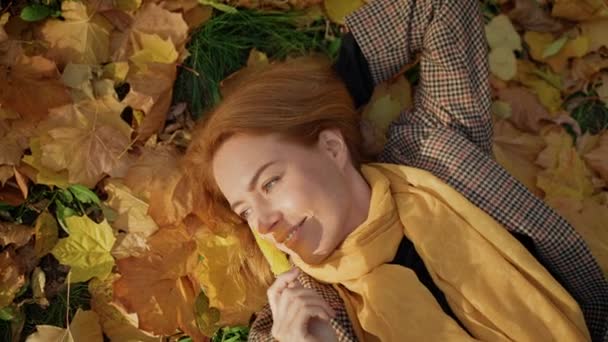 女性は秋の公園の葉の上に寝そべってカメラを覗き込んで — ストック動画