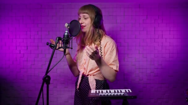 Női énekes a fejhallgatóban a stúdió felvételein szám mikrofonban — Stock videók